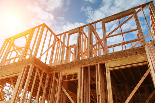 Wooden frame structure of a custom home under construction with exposed timber beams against a bright blue sky.