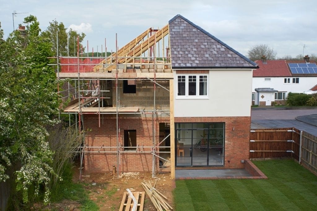 Two-storey house extension under construction with scaffolding, timber roof framework, brick exterior walls, and modern rear glazing during a residential home renovation project.