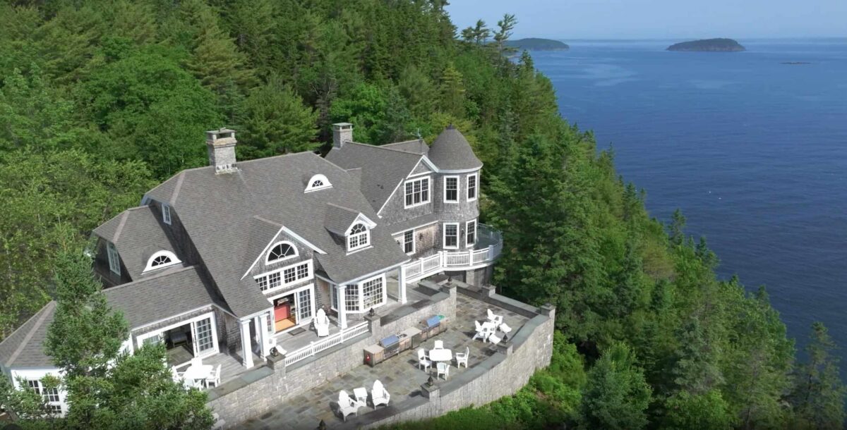 Luxury oceanfront estate with expansive stone terrace, panoramic water views, and private wooded setting.