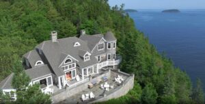 Luxury oceanfront estate with expansive stone terrace, panoramic water views, and private wooded setting.