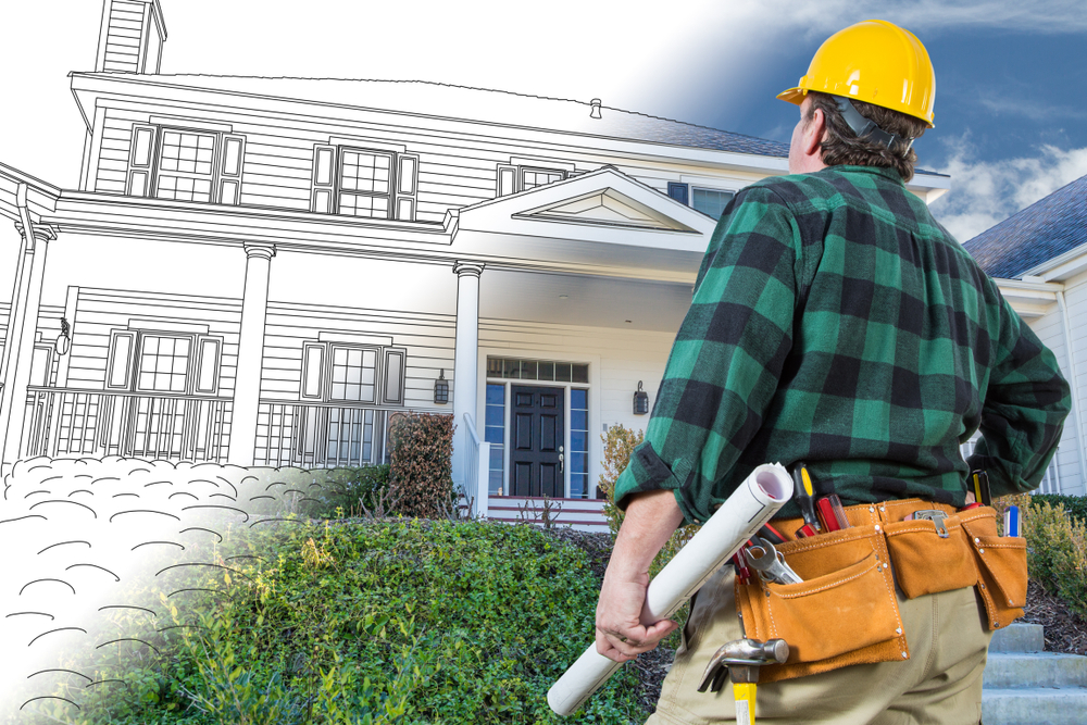 Construction worker in a yellow hard hat and tool belt examining a house, half rendered as architectural blueprint and half as a completed home, representing residential building design and renovation planning.
